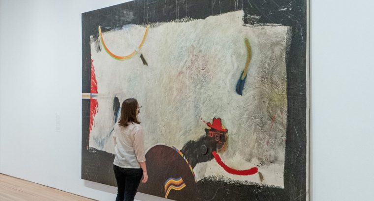 A woman wearing a mask standing in front of a large abstract artwork