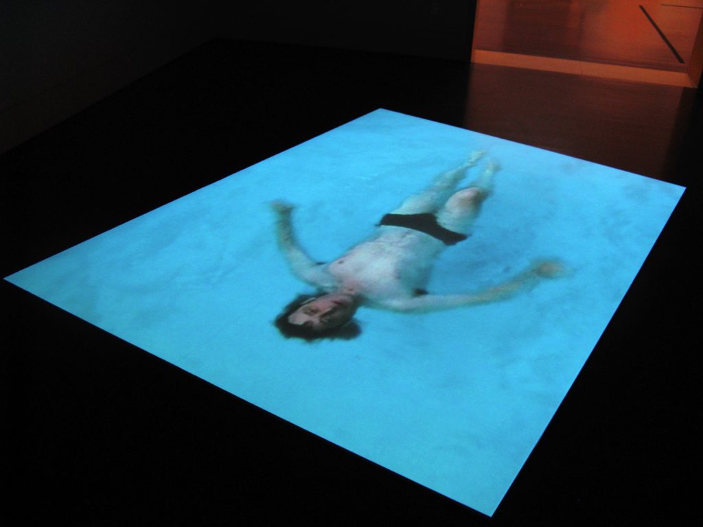 Video installation, of a male swimmer floating in water, projected onto the floor.