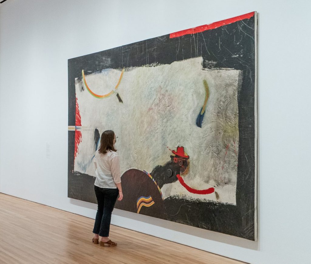 A woman wearing a mask standing in front of a large abstract artwork