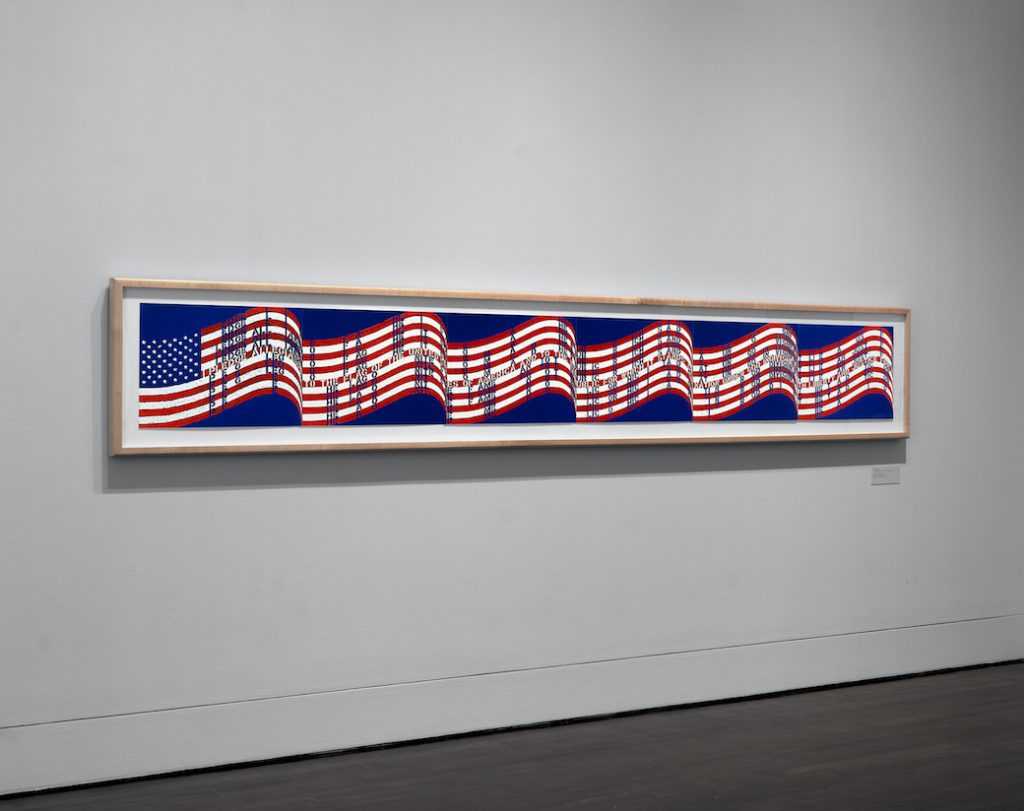A long horizontal artwork based on the USA flag hanging on a wall.